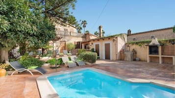 A swimming pool with lounge chairs, a stone building, and a garden area.