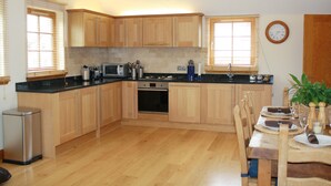 Une cuisine avec des meubles de rangement en bois, une cuisinière et une table à manger pour quatre personnes.