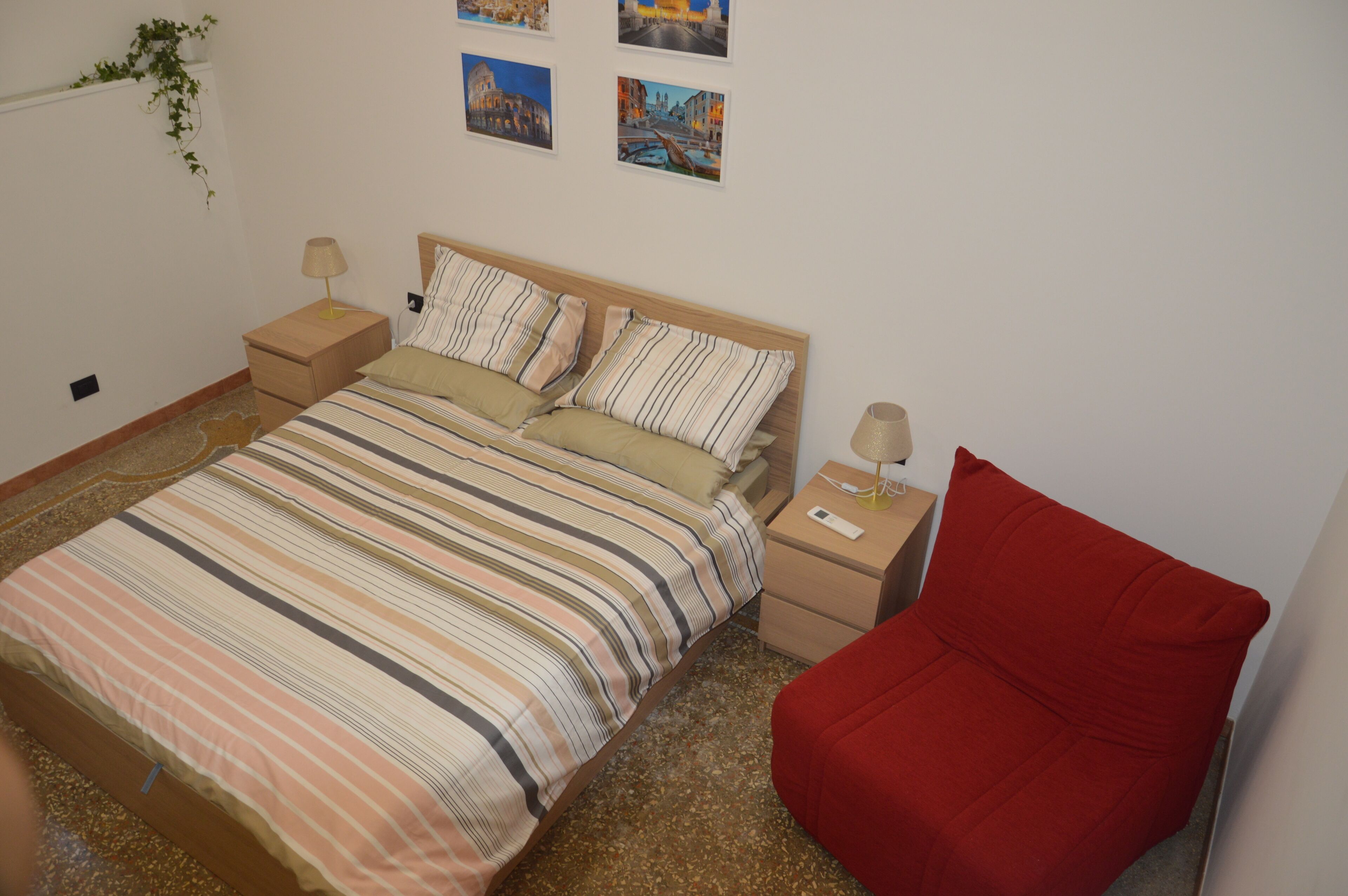 A bedroom with a bed, two bedside tables, a red chair, and wall art.