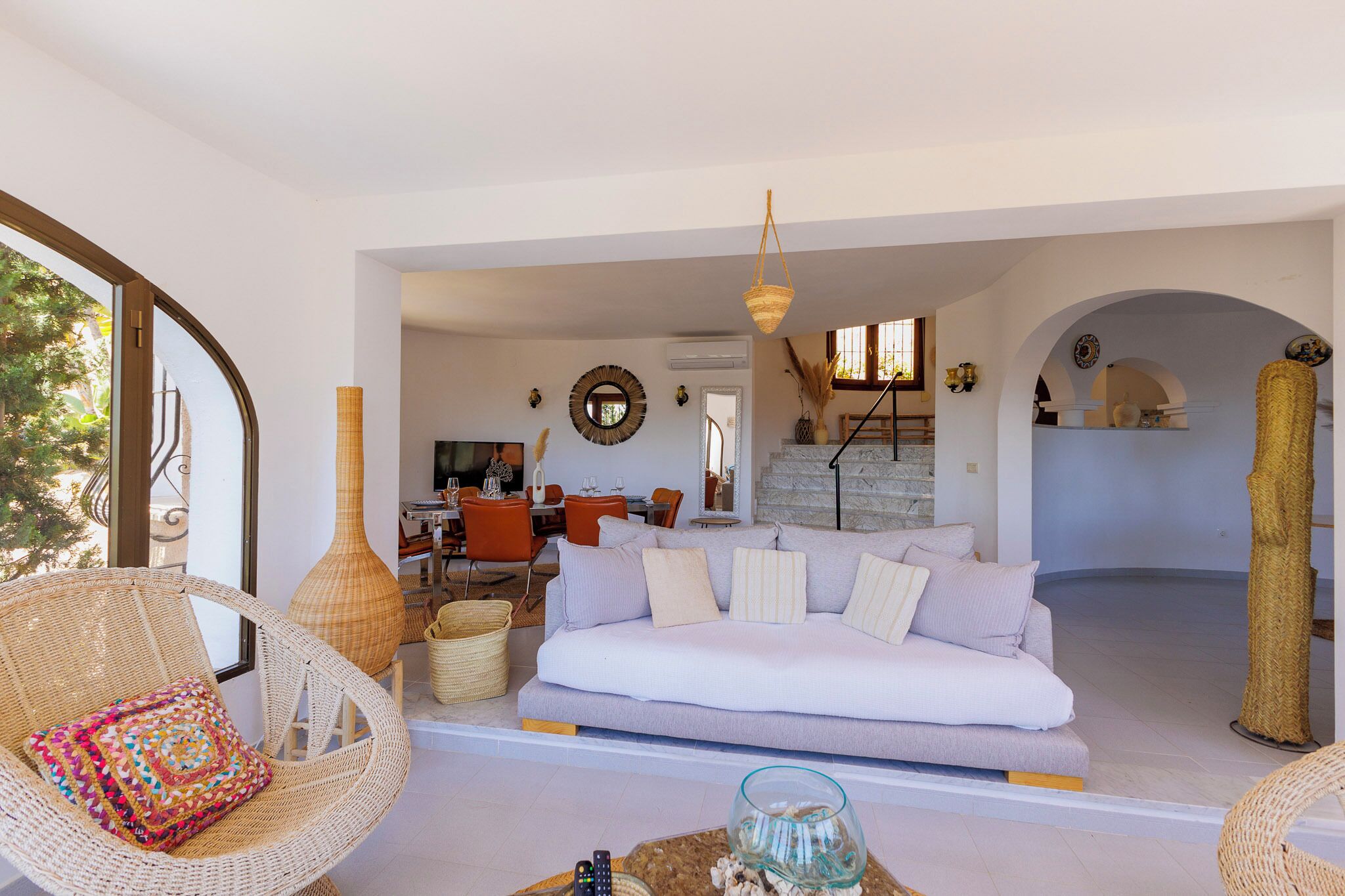 A spacious living area with a white sofa, wicker chairs, and a dining table.