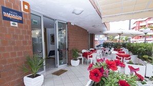 A hotel entrance with a sign, a glass door, and an outdoor seating area with tables and chairs.