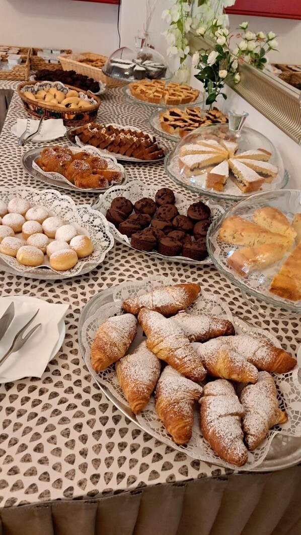 A table with various pastries and desserts, including croissants, muffins, and pies, arranged on a patterned tablecloth. - Hotel Napoleon (Riccione)