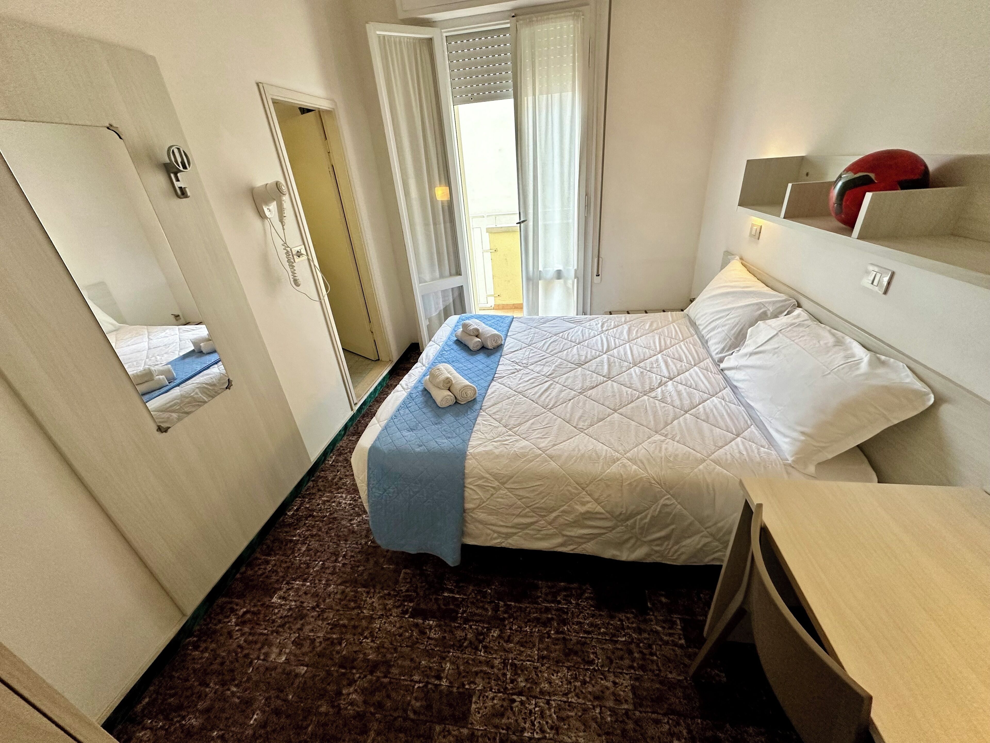 Ein Hotelzimmer mit einem Bett, einem Schreibtisch, einem Spiegel und einer Tür.