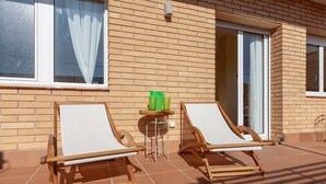 A patio with two wooden lounge chairs and a small table with green cups. - Spacious and bright designer apartment next to Playa Larga (Tarragona)