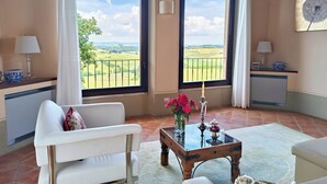 A room with a white sofa, a glass-top table with a vase of flowers, and two large windows offering a view of a green landscape. - Luxury Villa in Montepulciano - Private Heated Pool, Free WiFi, Magnificent view (Montepulciano)