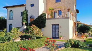A two-story house with a balcony, a small tower-like structure, and a garden with red flowers. - Luxury Villa in Montepulciano - Private Heated Pool, Free WiFi, Magnificent view (Montepulciano)