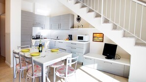 A modern kitchen with white cabinets, a dining table set for four, and a staircase leading to another level. - Lenno Spese II –Village apartment In Lenno with pool by Italian Apartments. (Lenno)
