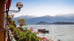 A lakeside view with mountains in the background, a boat on the water, and a balcony with outdoor seating. - Lenno Spese II –Village apartment In Lenno with pool by Italian Apartments. (Lenno)