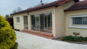 A single-story house with a tiled roof, a sliding glass door entrance, and a gravel driveway.
