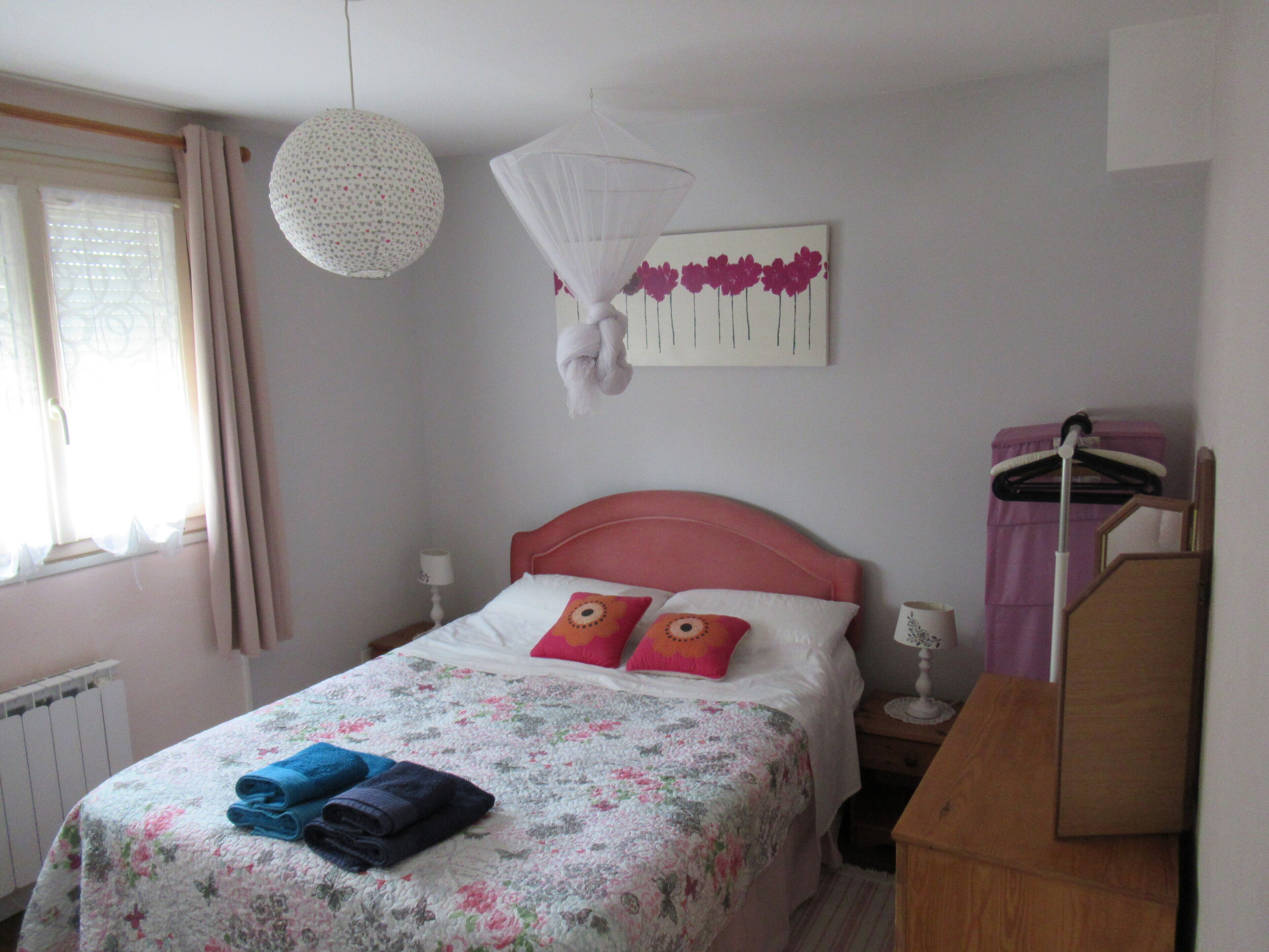 A bedroom with a floral bedspread, pink headboard, and a bedside table with a lamp.