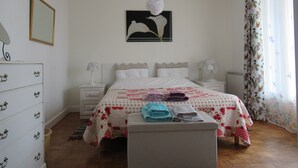 A bedroom with a bed, a dresser, a nightstand, a fan, a ceiling fan, and a window with curtains.