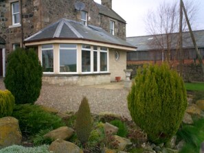 A stone building with a circular windowed structure, surrounded by rocks and shrubs. - Beautifully situated amidst rolling farmland (Scotland)
