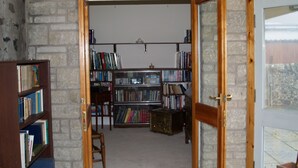 Une bibliothèque avec des étagères, une chaise en bois et un mur en pierre.