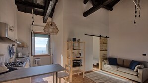 A modern kitchen with a dining area, a wooden bookshelf, and a sofa.