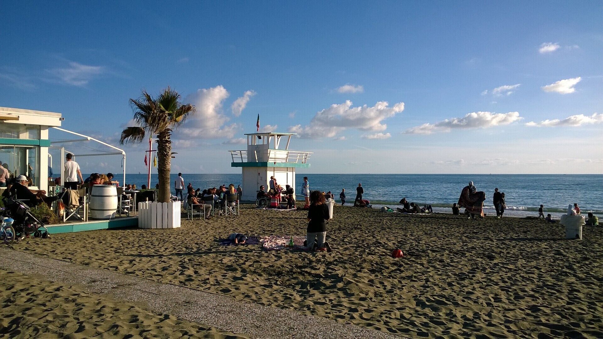 A beach with a lifeguard tower, a covered seating area, and people relaxing.
