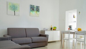 A modern living room with a grey sofa, a dining area with white chairs, and a kitchen in the background. - bright apartment fully restored (murano)