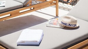 Une chaise longue, avec une serviette pliée et un chapeau à proximité, donnant sur une étendue d’eau, avec des montagnes à l’horizon.