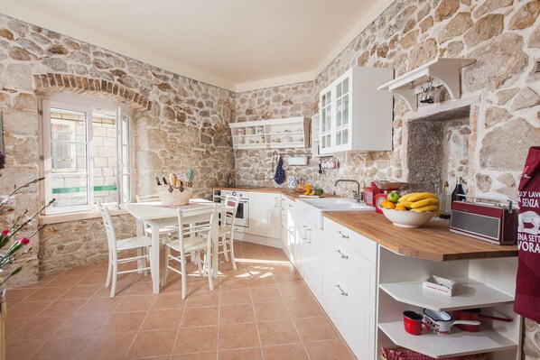 A kitchen with stone walls, white cabinetry, a wooden countertop, and a dining area with white chairs.
