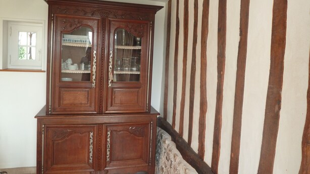Ein traditioneller Holzkabinet mit Glastüren, vor einer Wand mit freiliegenden Holzbalken platziert.