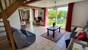 Ein geräumiges Wohnzimmer mit einer Holztreppe, einem schwarzen Ledersofa, einem Holztisch und Blick auf einen Garten durch große Fenster.