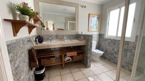 Une salle de bain avec deux lavabos, des toilettes, une douche et un grand miroir.