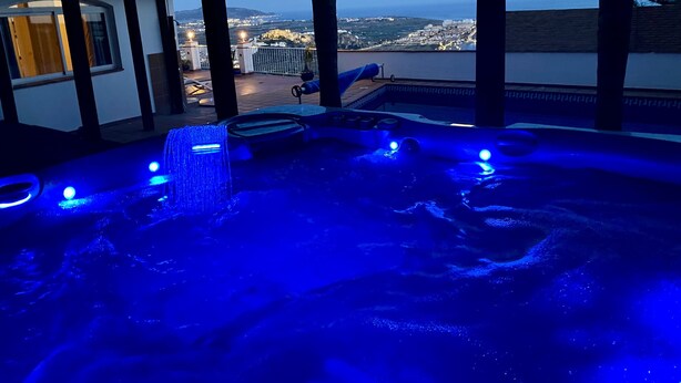 Un bain à remous avec un éclairage bleu, offrant une vue sur la ville au crépuscule.