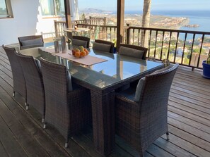 Un balcon agrémenté de meubles en osier, d’une table en verre et d’un saladier rempli de fruits.