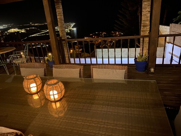 A night view from a balcony with a table, chairs, and two lit lanterns.