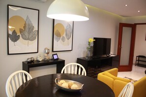 A modern living room with a dining area, featuring a round table with a bowl of decorative items, a sofa, a TV, and artwork on the wall. - Faro Stadium Flat @ City Center By Freetimealgarve (Faro)