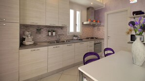 A modern kitchen with light wood cabinets, a built-in oven, and a dining area with a white table and purple chairs. - SPLENDIDA SINGLE HOUSE IN GATTEO MARE (Gatteo A Mare)