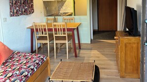 A compact living space with a sofa, dining table, chairs, a small TV, and a kitchen area.