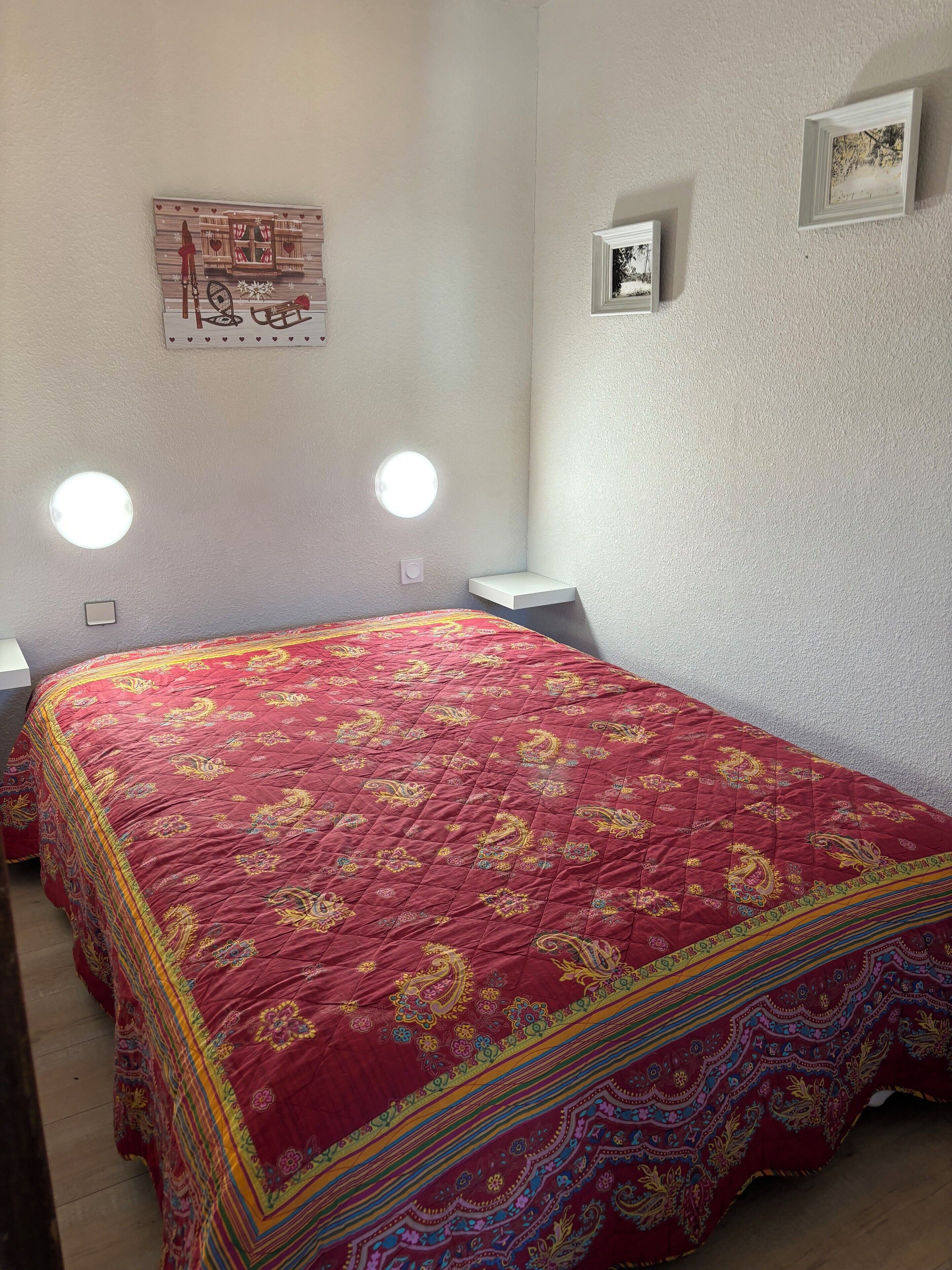 Un dormitorio con una colcha acolchada roja, dos mesitas de noche y un estante en la pared.