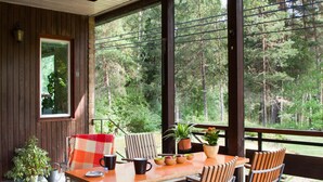 A covered outdoor seating area with a wooden table and chairs, potted plants, and a view of a forest. - 60ies house in Stockholm close to nature, International Fairs, S-malm and City (Stockholm)
