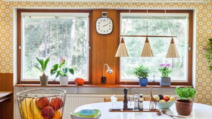 A kitchen with a large window, a fruit bowl, a clock, and various potted plants. - 60ies house in Stockholm close to nature, International Fairs, S-malm and City (Stockholm)
