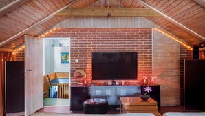 An attic room with a brick wall, a flat-screen TV, a wooden ceiling, and a cozy seating area with a bench and ottoman. - 60ies house in Stockholm close to nature, International Fairs, S-malm and City (Stockholm)