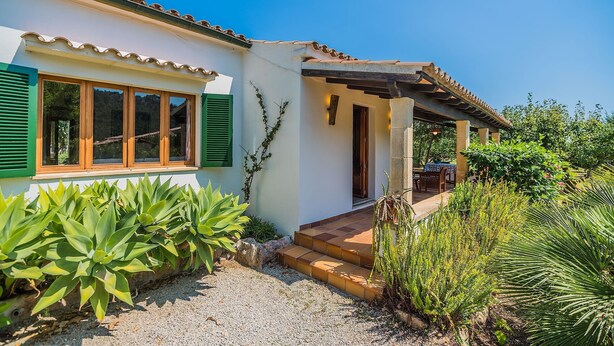 Ein Haus mit weißer Fassade, grünen Fensterläden und einer Veranda mit Tisch und Stühlen.