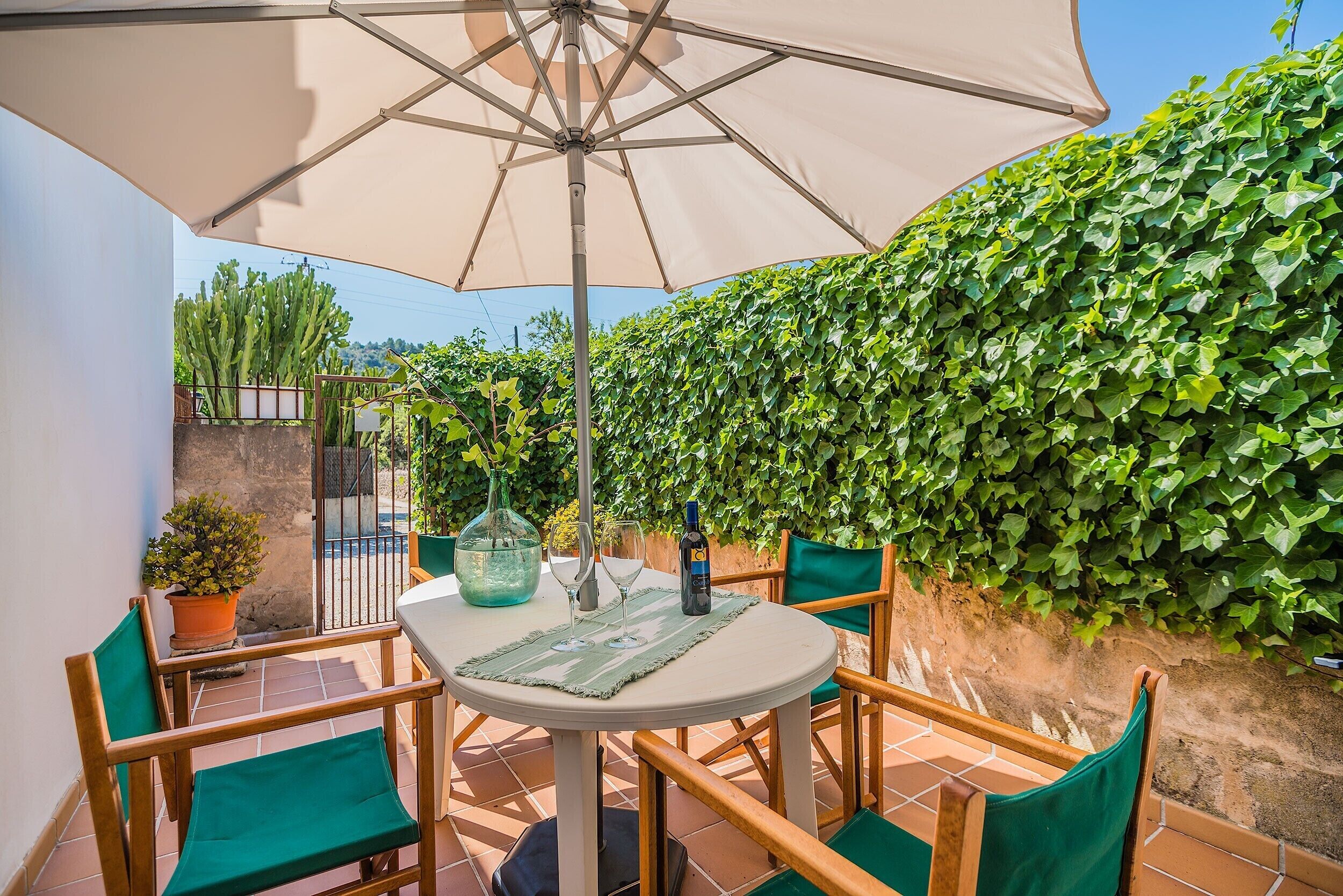 A patio with a round table, four chairs, a table umbrella, a potted plant, and a wine bottle.
