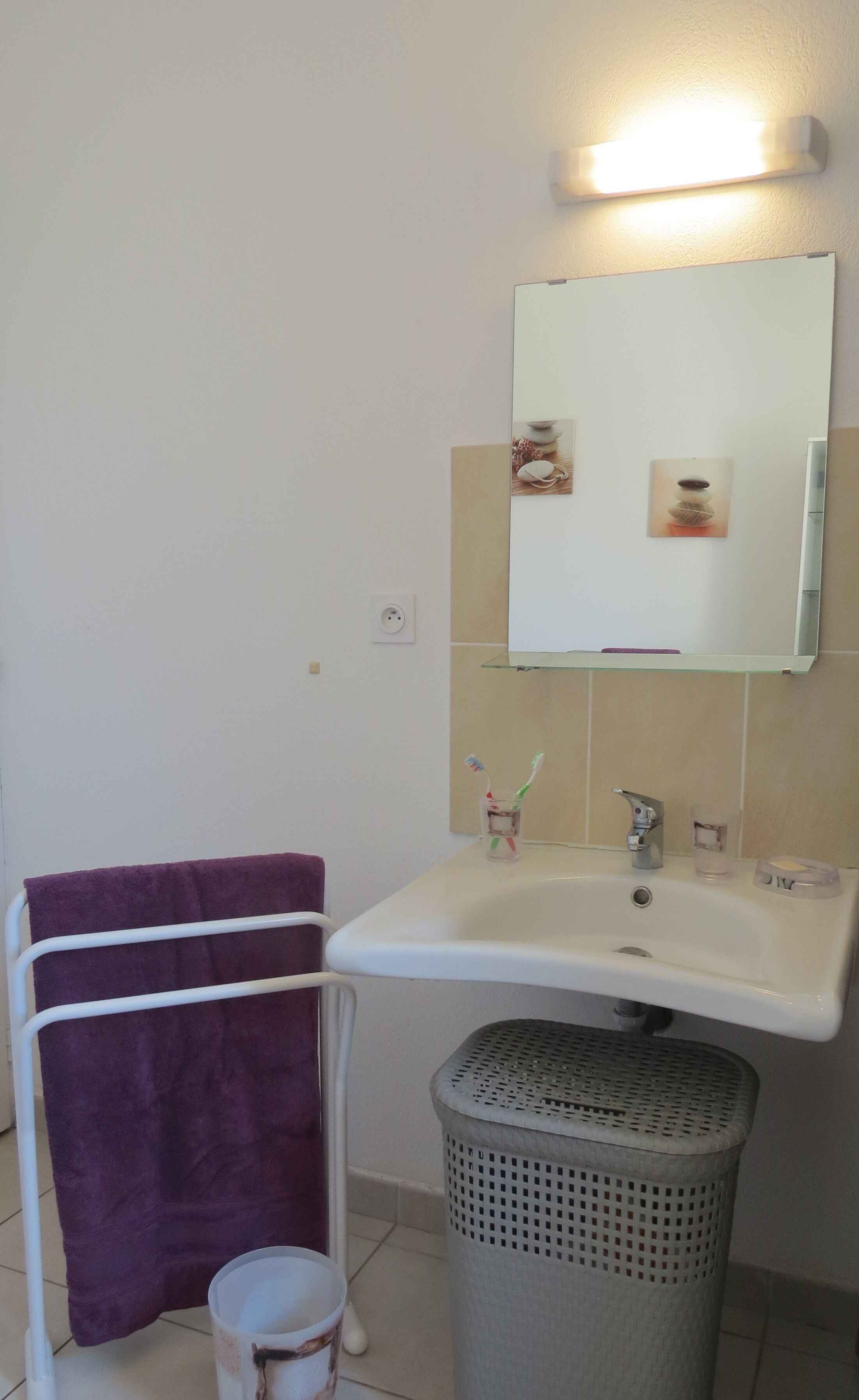 Un baño con un lavamanos blanco, un espejo y un cubo de basura.