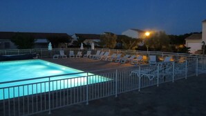 Una piscina con valla blanca, rodeada de sillas de descanso y sombrillas.
