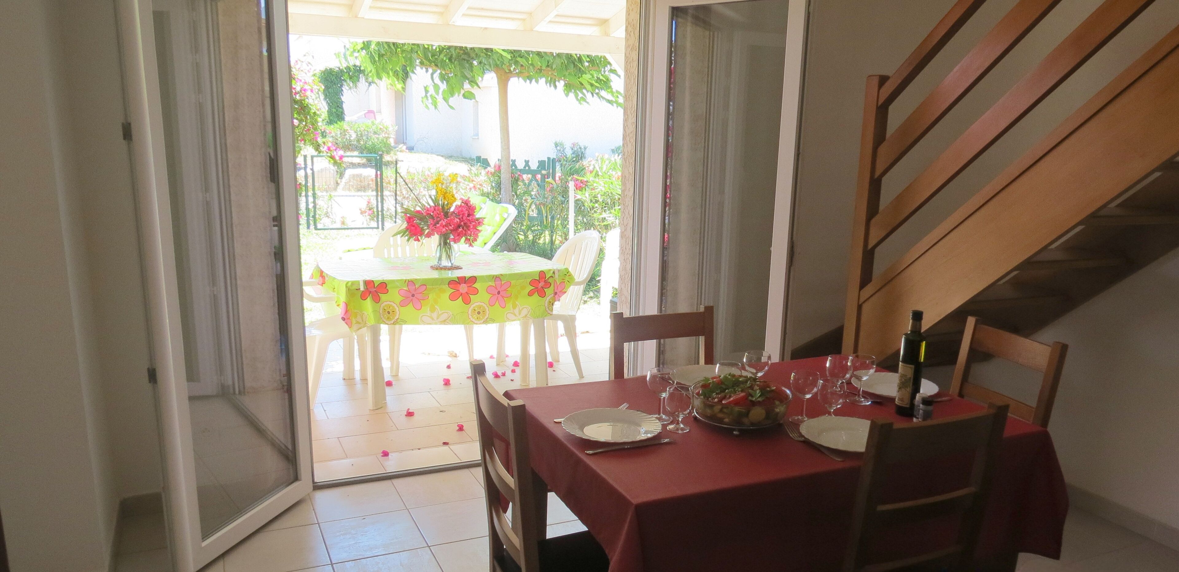 An open patio with a dining table set for two, a bottle of wine, and a bowl of salad.