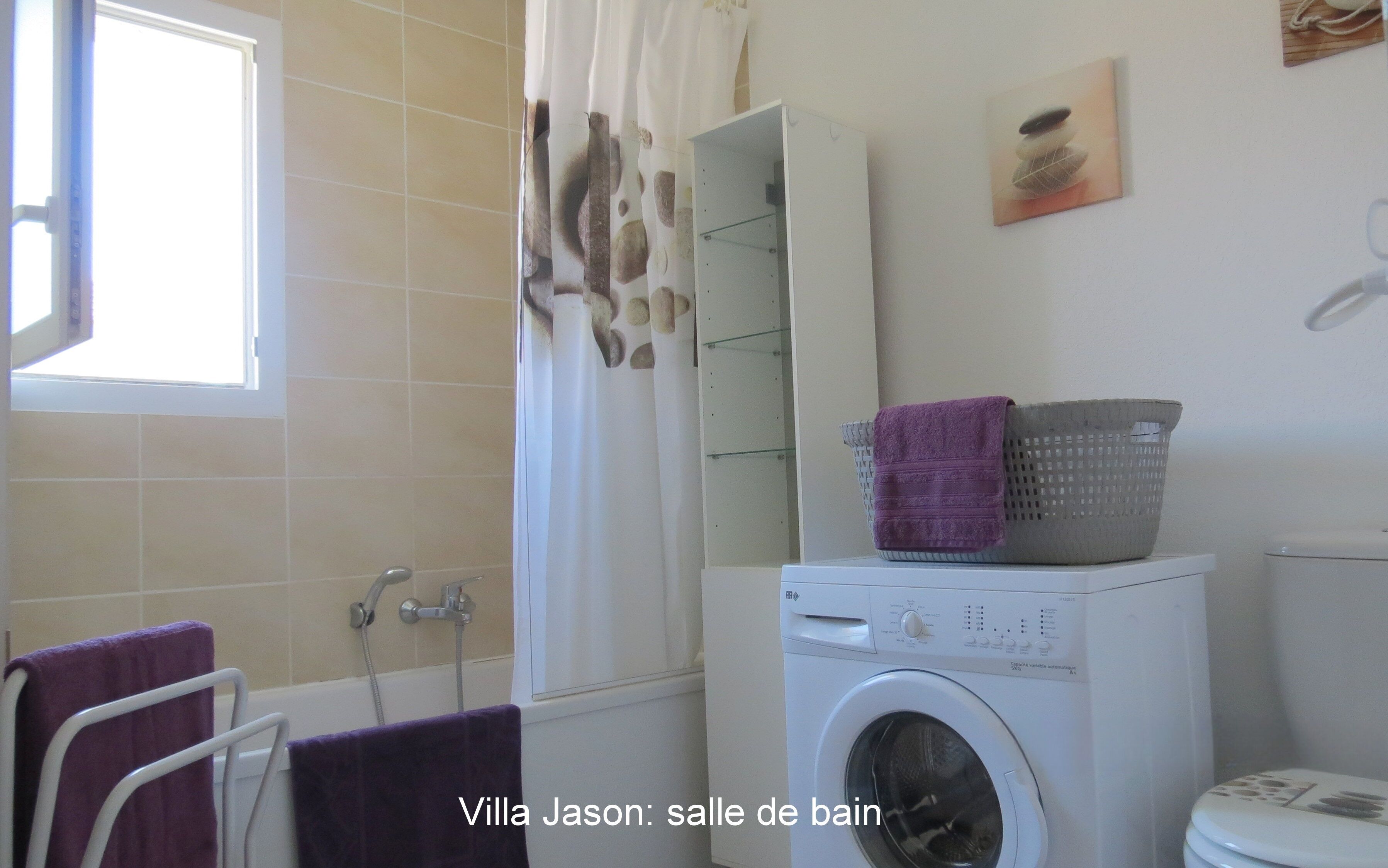A bathroom with a washing machine, a shower, and a window.