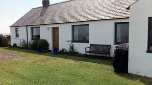 A white house with a tiled roof, a wooden door, and a bench outside. - Cottage With Secure Garden, Wood Burning Stove And Sea Views (St Cyrus)