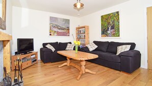 A living room with a wooden coffee table, black sofas, a bookshelf, and a television. - Cottage With Secure Garden, Wood Burning Stove And Sea Views (St Cyrus)