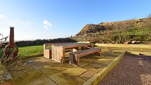 An outdoor patio with stone flooring, wooden benches, and a stone wall. - Cottage With Secure Garden, Wood Burning Stove And Sea Views (St Cyrus)