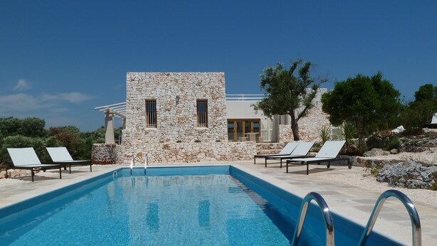 A swimming pool with lounge chairs, a stone building, and a clear sky. - Architecturally Designed Sea View Villa in Carovigno, Nr Ostuni with Heated Pool (carovigno)