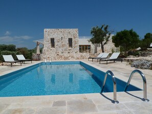 A swimming pool with lounge chairs, a stone building, and a clear sky.