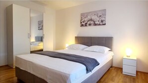 A neatly arranged bedroom with a bed, bedside tables, a wardrobe, and a painting on the wall.