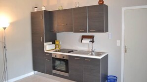 Cocina pequeña con armarios oscuros, horno empotrado, pileta y una mesada con tetera y cafetera.