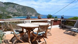 Un patio con una mesa redonda y sillas, con vista a un paisaje costero con acantilados y el mar.