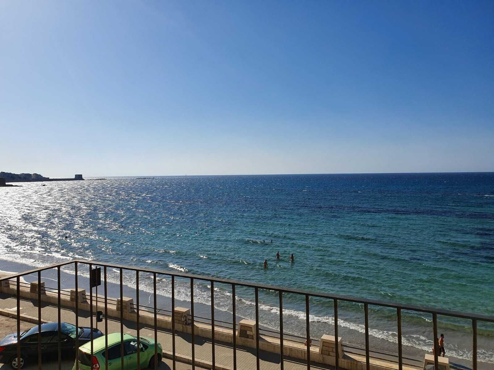 Blick auf die Küste mit blauem Himmel, einem Strand und einer Straße mit parkenden Autos.